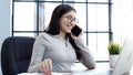 A young woman with glasses in the office is working on a laptop and talking on the phone Royalty Free Stock Photo