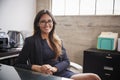 Young woman in glasses sits at office desk smiling to camera Royalty Free Stock Photo