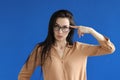 Young woman in glasses twirling her finger at temple on blue background