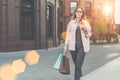 Young woman in glasses is walking along city street, carrying shopping bag and holding cup of coffee. Royalty Free Stock Photo