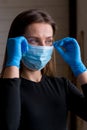Young woman in gloves puts on a medical mask near the window at home
