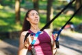 Young woman goes in for sports in the park with fitness belts. The athlete trains her back muscles