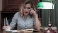 Young woman going through a book and having an angry phone conversation sitting at her desk Royalty Free Stock Photo