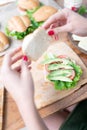 A young woman is going to close a healthy sandwich with lettuce, avocado and tomato at home