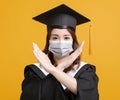 Young woman in graduation gowns with medical mask and showing stop gesture