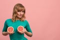 Young woman with grapefruit halves in her hands, cheerful girl in green posing at the camera with grapefruits on a pink