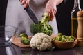 Young woman in a gray aprons cuts cauliflower broccoli