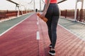 Young woman in gray pants standing on cinder track with bottle. Charming female runner waiting for