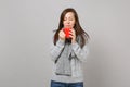 Young woman in gray sweater scarf with closed eyes hold red cup of coffee or tea isolated on grey background. Healthy Royalty Free Stock Photo