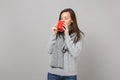 Young woman in gray sweater, scarf drinking coffee or tea from red cup isolated on grey background in studio. Healthy Royalty Free Stock Photo