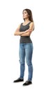 Young woman in gray top and blue jeans standing in half-turn with arms folded, looking up and away, isolated on white