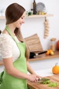 Young woman in the green apron cooking in the kitchen. Housewife slicing fresh salad Royalty Free Stock Photo