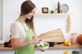 Young woman in the green apron cooking in the kitchen. Housewife slicing fresh salad. Royalty Free Stock Photo