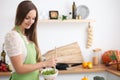 Young woman in the green apron cooking in the kitchen. Housewife slicing fresh salad. Royalty Free Stock Photo