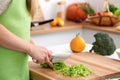 Young woman in the green apron cooking in the kitchen. Housewife slicing fresh salad Royalty Free Stock Photo