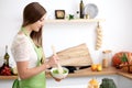 Young woman in the green apron cooking in the kitchen. Housewife slicing fresh salad Royalty Free Stock Photo