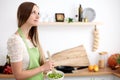 Young woman in the green apron cooking in the kitchen. Housewife slicing fresh salad Royalty Free Stock Photo