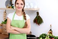 Young woman in green apron is going for cooking in a kitchen. Housewife is tasting the soup by wooden spoon.