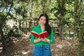 Young woman with a green blouse, enjoying reading a book in the shade of forest. World book day