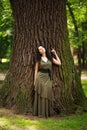 Young woman in green dress meditatively relaxes near large tree in forest park, concept of purity of nature and unity with Royalty Free Stock Photo