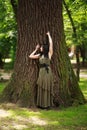 Young woman in green dress meditatively relaxes near large tree in forest park, concept of purity of nature and unity with Royalty Free Stock Photo