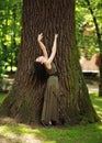 Young woman in green dress meditatively relaxes near large tree in forest park, concept of purity of nature and unity with Royalty Free Stock Photo