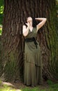 Young woman in green dress meditatively relaxes near large tree in forest park, concept of purity of nature and unity with Royalty Free Stock Photo