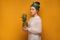Young woman with a kerchief holds a pineapple, yellow background