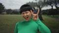 Young woman in green making rock and roll gesture outdoors in a green park with a playful expression Royalty Free Stock Photo