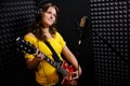 A young woman with a guitar in a recording Studio. A girl with an electric guitar stands with a microphone. Record musical Royalty Free Stock Photo