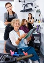 Young woman hairdresser in hair salon helping to senior woman ch