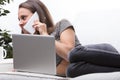 Young woman on couch, half-lying with laptop, phone delivering f Royalty Free Stock Photo