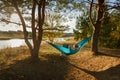 Young woman in hammok relax while working with laptop outdoor, facing lake on a sunset Royalty Free Stock Photo