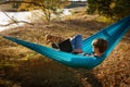 Young woman in hammok using laptop working outdoor facing lake on a sunset together with her home pet dog Royalty Free Stock Photo