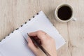 Young woman hand hold opened notebook pages with black pen next to cup of coffee on  wooden table. Top view Royalty Free Stock Photo