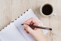 Young woman hand hold opened notebook pages with black pen next to cup of coffee on  wooden table. Top view Royalty Free Stock Photo