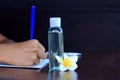 Young woman hand holding blue pen writing on book, transparent hand sanitizer gel oil, white Bali frangipany flower on desk . Royalty Free Stock Photo