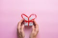 Young Woman Hand Holding Gift Box with Red Ribbon in Heart Shape on Pink Background. Overhead View Flat Lay. Valentine Royalty Free Stock Photo