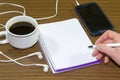 Young woman hand holding smartphone and pen writing on notebook paper at coffee shop. Royalty Free Stock Photo