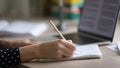 Young woman hands making notes in copybook by computer screen