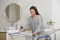 Young woman hanging clean laundry on drying rack in bathroom