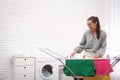 Young woman hanging clean laundry on drying rack indoors