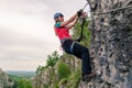 Young woman hanging from a via ferrata cable, while passing a difficult section, equipped with helmet, harness, kit.