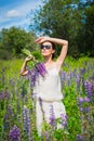 Young woman, happy, standing among the field of violet lupines, smiling, purple flowers. Blue sky on the background. Summer, with Royalty Free Stock Photo