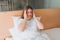 Young Woman with hard headache holding hands on head. She is sick, sitting alone on bed at home. Covid-19 new variant - Royalty Free Stock Photo