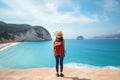 Young woman in a hat with a backpack standing on the edge of a cliff and looking at the sea, Young woman with backpack on the Royalty Free Stock Photo