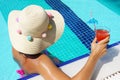 Young woman with hat and colorful swimsuit drinking cocktail at swimming pool Royalty Free Stock Photo