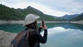 Young woman in hat films lake and mountains in Spain with phone, slomo