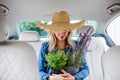 Young woman with hat and plants sitting in car, having fun.