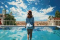 Young woman in hat and shirt standing near swimming pool with city view, A tourist woman rear view in a swimming pool enjoys the Royalty Free Stock Photo